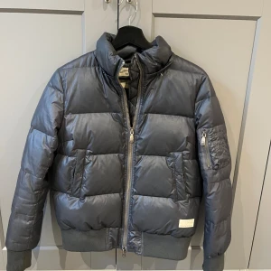 Mörkgrå pufferjacka från Stone Island - Säljer en mörkgrå pufferjacka från Stone Island med hög krage, breda quiltade paneler och dragkedja framtill. Jackan har ribbade muddar, fickor med lock och dragkedja på ärmen. Pris får att diskutera🥰lite osäker på storleken men tror s-m ❤️