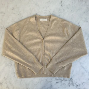 Beige kofta från Zara med v-ringning - Beige kofta från Zara med v-ringning och knappar framtill. Långärmad modell i mjukt stickat material, perfekt för lager-på-lager. Klassisk och enkel design som funkar till allt. Ribbstickade muddar vid ärmslut och nederkant.