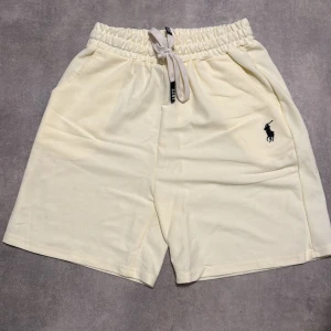 Polo Ralph Lauren ljusgula shorts - Snygga ljusgula shorts från Polo Ralph Lauren med broderad logga på vänster ben. De har elastisk midja med snörning och två sidofickor. Perfekta för sommardagar och chill vibes. Mjukt bomullsmaterial för extra komfort.