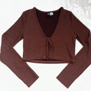 Brun croppad ribbad bolerotopp från H&M - Säljer en brun croppad bolerotopp från H&M. Toppen är ribbad, har lång ärm, v-ringning och knyt framtill. Superfin färg och som ny 🥰