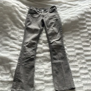 Grå bootcut jeans - Snygga grå jeans med bootcut passform och klassiska fem fickor. Baktill finns fickor med lock och silverfärgade knappar. Jeansen har bälteshällor och är tillverkade i ett mjukt bomullsmaterial med lite stretch. Perfekta för en avslappnad och trendig look. Storlek 152 för 11-12 år. Inga defekter!