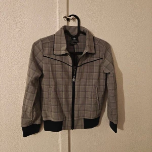 LCEE bomberjacka - Snygg bomberjacka från LCEE i limited edition med klassiskt rutigt mönster i grått och svart. Jackan har svart dragkedja, ribbade muddar och krage med kontrastkant. Perfekt för dig som gillar streetstyle och vill sticka ut med en unik look. .  Nytt med lappen kvar. Jag kan inte se några hål eller skador etc. Även om de är nytt.  Obs! Jag står inte för frakbolagets slarv, skador eller annat som händer efter att jag har postat.