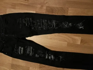 Svarta ripped jeans från Dsquared2 - Svarta jeans från Dsquared2 med kraftiga slitningar och trasiga detaljer framtill. Modellen är slim och har klassisk femficksdesign. Jeansen är tillverkade i bomull och har en modern, edgy look som sticker ut.