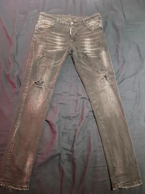 Svarta skinny jeans från Dsquared2 - Svarta jeans från Dsquared2 med slitna detaljer och snygga hål på framsidan. Skinny fit med fem fickor och coolt Dsquared2-märke baktill i vitt och gult. Jeansen har en mörk tvätt och är tillverkade i klassiskt jeansmaterial.