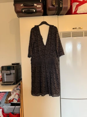 Svart kortklänning med stjärnmönster - Svart kortklänning med djup v-ringning och trekvartsärm. Klänningen har ett broderat stjärnmönster, spetsdetaljer längs kanterna och midjeband med knyt. Materialet är lätt och genomskinligt, perfekt för dig som gillar unika detaljer och en cool look. Storlek 1 som enligt deras storleksguide motsvarar en S. Men den är rymlig i storlek. Kanske en S/M. Mycket fint skick, jag hittar inga synliga anmärkningar eller defekter. 