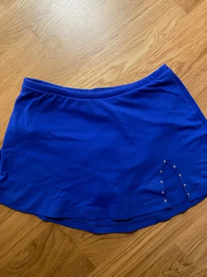 Blå konståkningskjol från bolero!! - Säljer en blå skort från Bolero med elastisk midja och snygga silvriga nitar vid slitsen. Materialet är mjukt och stretchigt, tillverkat av 85% polyamid och 15% elastan. Perfekt för dig som gillar sportig och bekväm stil.!! Säljer pga att den är för liten för mig!!