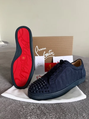 Christian Louboutin skor  - Säljer ett par mörkblå sneakers från Christian Louboutin med ikonisk röd sula och svarta nitar på tån. Skorna har snörning och är tillverkade i mocka med läderfoder. Snygg och edgy design som sticker ut med detaljerna framtill.