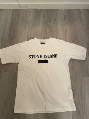 Vit Stone Island t-shirt med tryck - Vit t-shirt från Stone Island i storlek M med klassiskt svart tryck på bröstet. Rund hals och korta ärmar. Materialet är mjuk polyester som känns skönt mot huden. Perfekt för dig som gillar clean och stilren streetwear med tydlig logga.