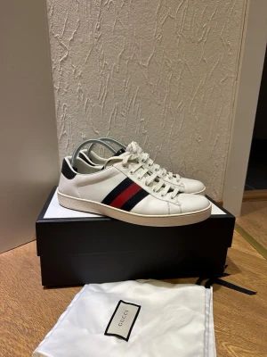 Gucci ace sneakers - Säljer ett par vita Gucci sneakers i skinn med klassiska ränder i rött och mörkblått på sidan. Alla orginaltillbehör följer med inklusive kvitto på över 6000kr. Storlek 44