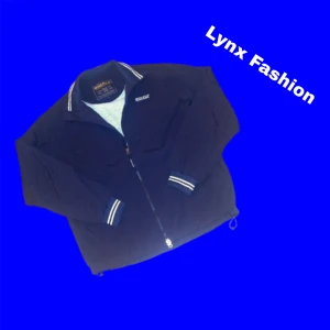 Mörkblå  vindjacka från Woolrich - Svart vindjacka från Woolrich med hel dragkedja och ståkrage. Jackan har vita ränder på mudden vid ärmslut och insidan av kragen, samt diskret logga på bröstet. Tillverkad i lätt polyester, perfekt för blåsiga dagar. Snygg och enkel design med normal passform.