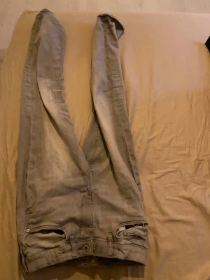 Grå jeansbyxor med raka ben - Säljer ett par grå jeansbyxor med klassisk femficksdesign och raka ben. Byxorna har knappstängning och dragkedja framtill. Perfekt för dig som gillar en enkel och avslappnad stil. Materialet är jeans och färgen är en ljusgrå ton.