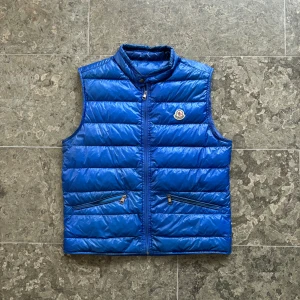 Moncler ”Gui” Väst - Säljer denna snygga moncler gui väst! | Storlek 4, passar medium/large | Skick: 7/10, lite skavanker. Se bilder. | Pris: 1799kr | Garanterar alltid äkthet på alla våra varor.