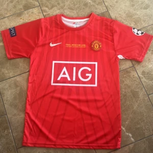 Manchester United Ronaldo 7 Nike tröja - Manchester United fotbollströja från Champions League-finalen 2008 med Ronaldo 7 på ryggen. Röd med subtila ränder, AIG-logga på bröstet, klubbmärke och Nike Swoosh. Kortärmad och tillverkad i Dri-FIT-material som andas. Champions League-patch på ärmen.