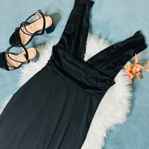 Svart långklänning med v-ringning - Svart långklänning med djup v-ringning och ärmlös design. Klänningen har en slits framtill som ger en snygg touch och är tillverkad i ett mjukt, följsamt material som sitter skönt mot kroppen. Perfekt för dig som gillar stilrena och eleganta plagg.