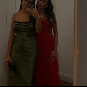 Grön satin balklänning med drapering - Säljer en elegant grön långklänning i satin med draperad effekt över byst och midja. Klänningen har en axelbandslös design och figurnära passform, perfekt för speciella tillfällen. Endast använt engångs🤍 Storlek Xs-S