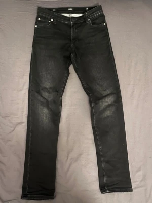Svarta slim jeans från Jack & Jones - Svarta jeans från Jack & Jones i slim fit-modell med klassisk femficksdesign och snygga slitningar på benen. Jeansen har normal midja och raka ben, tillverkade i mjukt bomullsmaterial med stretch för extra komfort. Perfekt för dig som gillar stilrena och bekväma jeans.