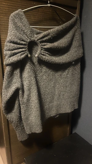 Grå offshoulder stickad tröja Zara - Säljer en grå stickad offshoulder tröja från Zara i storlek S. Tröjan har en unik detalj framtill med rynkad design och två dekorativa pärlor. Materialet är mjukt och lite fluffigt, perfekt för kyliga dagar. Passformen är loose och ger en avslappnad vibe. Finns ej att köpa längre.