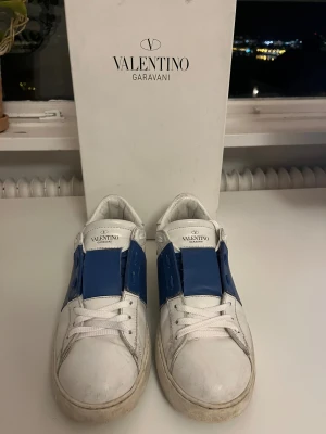 Valentino Garavani Open sneakers vit/blå - Snygga Valentino Garavani Open sneakers i vitt skinn med bred blå läderdetalj över sidan. Storlek 41. Hör av dig om du har några funderingar 