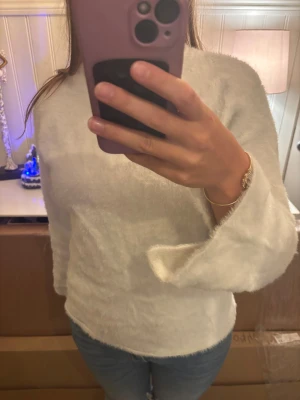 Vit fluffig långärmad tröja - Supermjuk och fluffig vit tröja med lång ärm och rund hals. Perfekt för dig som gillar en mysig och enkel stil. Tröjan har en normal passform och är tillverkad i ett syntetmaterial som känns riktigt skönt mot huden.