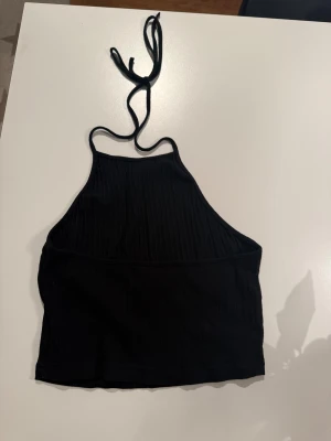 Svart ribbad linnetopp med knyt - Säljer en svart ribbad linnetopp med smala axelband som knyts i nacken. 