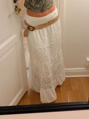 Vit långkjol med skärp  - Säljer en vit långkjol med snygga spetsdetaljer och ett flätat bälte som tillhör. Har köpt kjolen i en butik i Köpenhamn men kommer tyvärr inte ihåg vad butiken hette. 