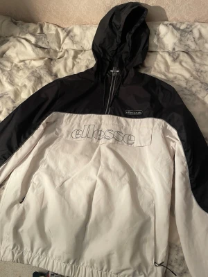 Ellesse svartvit tracksuit set M - Säljer ett fräscht tracksuit set från Ellesse i storlek M. Jackan har svart huva och axlar, vit kropp med stor Ellesse-logga och half zip. Byxorna är vita med svarta detaljer vid fickorna och Ellesse-märke. Materialet är syntet och har en sportig vibe.