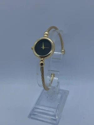 damklocka med ett vackert guldfärgat armband - 🟠 KÖP 2 FÅ 1 PRESENT 🎁. ✅Nytt Batteri 🔋  Säljer en elegant damklocka med ett vackert guldfärgat armband. Klockan har en stilren design med en mörk urtavla och guldfärgade detaljer. Perfekt accessoar för både vardag och fest. Gjorde i rostfritt stål  Jag har en i silver också, så kontakta mig om du vill köpa den!   Klockhållaren kommer inte med.