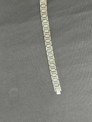 Silverfärgad armbandslänk från Lacoste - Snygg armbandslänk i silverfärgat metall från Lacoste med rektangulära länkar och diskret rutmönster. Länken har en platta med Lacoste-loggan och känns både stilren och modern. Perfekt för dig som gillar accessoarer med lite edge.