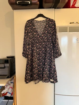 Blommig svart kortklänning med v-ringning - Supersöt svart kortklänning med blommigt mönster i rosa och vitt. Klänningen har v-ringning, trekvartsärm och ett flowy fall. Perfekt för dig som gillar en romantisk och avslappnad stil. Materialet känns lätt och luftigt. Från märket Odd Molly. Storlek 2 som enligt deras storleksguide motsvarar en M. Mycket fint skick, jag hittar inga synliga anmärkningar eller defekter.  