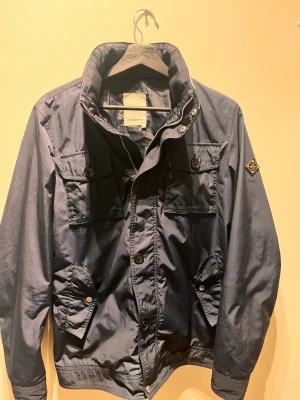 Blå fieldjacket från J.Lindeberg - j.lindeberg fieldjacket i väldigt bra skick, denna jacka är av den äldre versionen vilket innebär att den har den sällsynta patchen på vänster jackärm. Som är väldigt eftertraktat! Storlek S men sitter som en lite mindre M. Först till kvarn!!