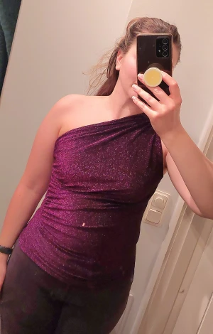 Lila glittrig topp - Enaxlad lila, glittrig topp med veckad söm i sidan och vid axeln. Elastisk och festlig! Stl. S, men passar också mig som har M. 