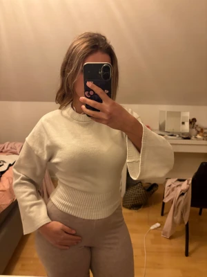 Vit stickad tröja med vida ärmar, wide sleeve knitted top - Säljer en vit stickad tröja med bred ribbad midja och vida, långärmade ärmar. Tröjan har en rundad halsringning och är i mjukt material som känns skönt mot huden. Perfekt för dig som gillar stilrena och enkla plagg med lite extra detalj på ärmarna. Nypris 400kr.