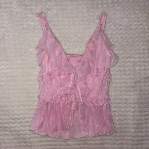 Rosa volangtopp från Amisu - Supersöt rosa linnetopp från Amisu med volanger och tunna axelband. Toppen har omlottkänsla framtill och flera lager av plisserade volanger som ger en romantisk vibe. Perfekt för dig som gillar en feminin och lekfull stil.
