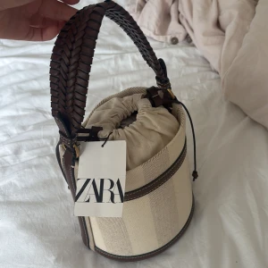 Beige och brun bucket bag från Zara - Snygg bucket bag från Zara. ALDRIG använd därav prislappen på och papper i väskan. 