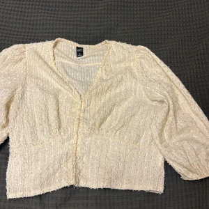 Beige blus med knappar från shein - Supersöt beige blus från Shein med v-ringning och knappar framtill. Blusen har ett diskret blommigt mönster, lätt puffade ärmar och är tillverkad i ett strukturerat tyg som ger en romantisk känsla. Perfekt att styla med jeans eller kjol!