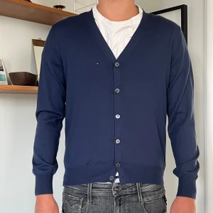 Marinblå kofta från Gran Sasso - Snygg marinblå kofta/cardigan från Gran Sasso i virgin wool. Tillverkad i Italien. Det finns tyvärr ett litet hål på höger bröst som också syns i bilderna.