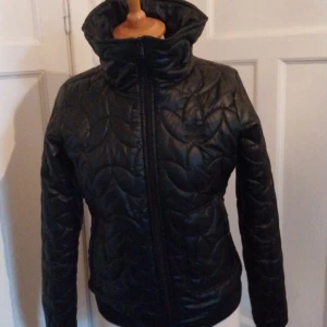 Svart quiltad pufferjacka från Adidas - Säljer en svart quiltad pufferjacka från Adidas med hög krage och dragkedja framtill. Jackan har ett snyggt mönster i sömmarna och broderad Adidas-logga på bröstet. Perfekt för kyliga dagar och riktigt skön att bära.