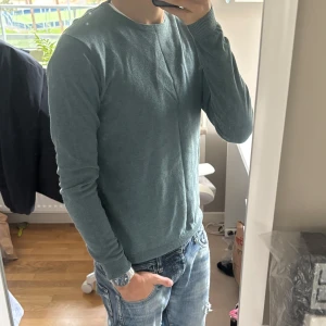 Grön långärmad tröja i bomull - Snygg grön långärmad tröja med rund hals och ribbade muddar. Enkel och stilren design som funkar till jeans eller andra favoritplagg. Mjuk och skön bomullskvalitet, perfekt för dig som gillar en clean look.