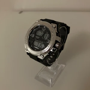 Sportig digital klocka silver/svart - Tuff digital sportklocka med svart urtavla och silverfärgad boett. Klockan har både analog och digital display, flera knappar för funktioner som alarm och timer samt blå bakgrundsbelysning. Armbandet är svart och robust, perfekt för dig som gillar en sportig stil.                                                                                       ✅Frakt inom 24 timmar 📦.                                                         ✅Nytt batteri 🔋.    
