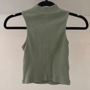 Ribbad ljusgrön ärmlös topp - Snygg ljusgrön polotopp i ribbat material. Toppen är ärmlös och har en hög krage som ger en trendig look. Perfekt att styla med jeans eller kjol för en snygg outfit! Använd någon enstaka gång så fint skick. Storlek XS/S