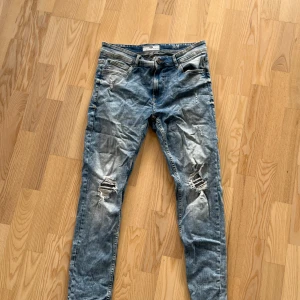 Blå slitna jeans från FSBN, 33/30 - Säljer ett par blå jeans från FSBN med slitningar och hål på båda knäna. Jeansen har klassisk femficksdesign, normal passform och är tillverkade i denim. Perfekta för dig som gillar en avslappnad och trendig look.