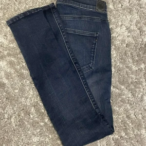 Slim fit Replay jeans i blå  - Snygga blå jeans från Replay med klassisk femficksdesign och tydliga kontrastsömmar. Jeansen har slimfit passform och raka ben, tillverkade i slitstarkt denim med Replay-logga på fickan. Perfekta för dig som gillar en tidlös och stilren look.