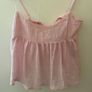 Ljusrosa linnetopp med rosett från Nelly - Supersöt ljusrosa linnetopp från Nelly med tunna axelband och volangliknande nederdel. Toppen har en snygg knytrosett i ryggen som ger en extra detalj. Perfekt för varma dagar och enkel att matcha med jeans eller kjol.