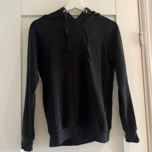 Svart hoodie från Gina Tricot XXS - En klassisk svart hoodie från Gina Tricot i storlek XXS. Tröjan har huva med snörning, långa ärmar och ribbade muddar vid ärmslut och nederkant. Perfekt för en chill och avslappnad stil.