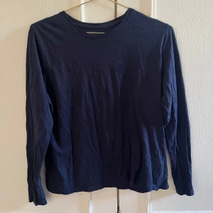 Mörkblå långärmad bomullströja - En basic mörkblå långärmad tröja i mjuk bomull. Tröjan har rund halsringning och en enkel, rak passform som funkar till det mesta. Perfekt att slänga på sig när det är lite kyligare ute.
