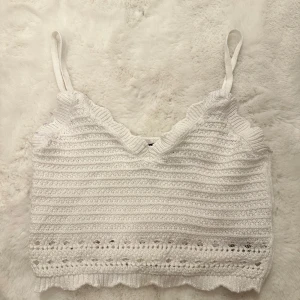 Vit stickad linnetopp från Gina Tricot - Supersöt vit stickad linnetopp från Gina Tricot med smala justerbara axelband och v-ringning. Toppen har virkade detaljer och vågig kant nertill, perfekt för en fräsch och somrig look. Passar till både jeans och kjol!