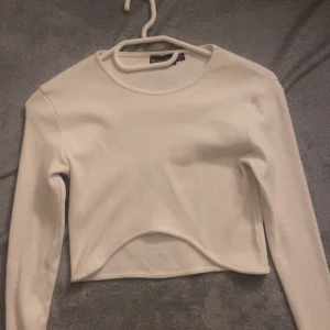 Vit croppad långärmad topp - Säljer en vit croppad långärmad topp från PrettyLittleThing. Toppen har en rund halsringning och är tillverkad i ett ribbat material som ger en snygg och bekväm passform. Perfekt att styla med jeans eller kjol för en trendig look.