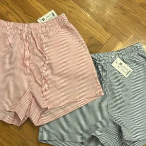 Randiga shorts med snörning helt nya!! - Fräscha randiga shorts från Lager157 i bomull, i både ljusblått och ljusrosa. De har elastisk midja med snörning och avslappnad passform. Perfekta för varma sommardagar och chill hemma. Snyggt mönster och mjukt material gör dem superbekväma.