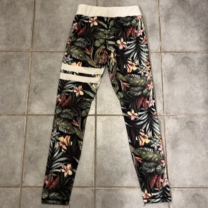 Stronger leggings med blommigt mönster - Säljer mina Stronger byxor  med tropiskt blommigt mönster i grönt, rosa, gult och vitt. Hög midja och perfekta för träning eller chill. Materialet är stretchigt och mjukt syntet. NYPRIS 799kr✨
