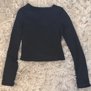 Svart långärmad topp i polyester - En stilren svart långärmad topp i stretchigt material med rund hals. Tillverkad av 95% polyester och 5% elastan, vilket gör den mjuk och följsam. Perfekt att matcha med jeans eller kjol för en clean look. Aldrig använd 